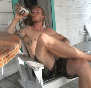 A beach bum drinking rum from the bottle at a shack on the beach in Belize